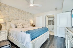 Una camera da letto con un letto, comodini, una ventola a soffitto, una porta del bagno e un comò.