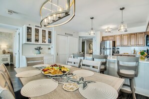 A modern kitchen with white cabinets, stainless steel appliances, and a dining area with a large table set for a meal. - 3BR 12th fl South Oceanview |Short walk to beach (North Myrtle Beach)