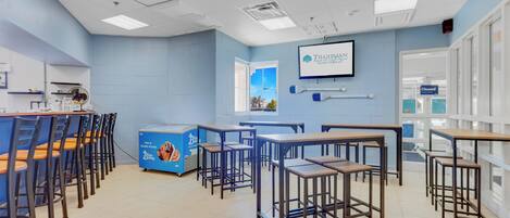 A classroom with blue walls, white ceiling lights, and a window with a view.