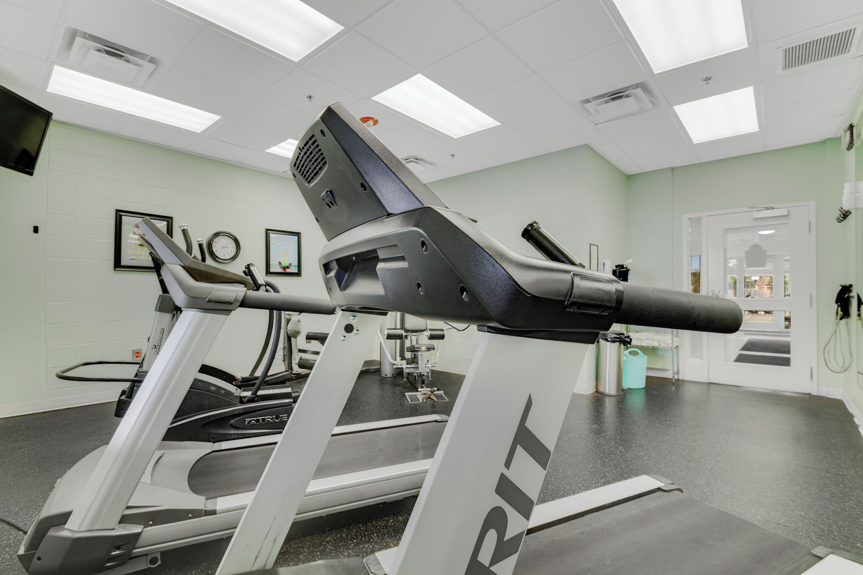 A gym with treadmills, exercise equipment, and a white wall with framed pictures.