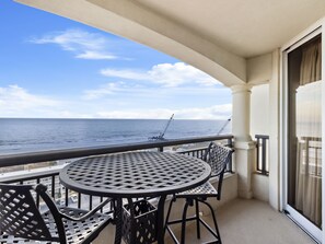 Un balcon avec une table ronde et des chaises, d’où l’on peut admirer la mer et apercevoir des grues au loin.