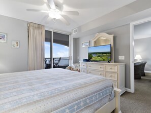 Une chambre dotée d’un grand lit, d’un ventilateur de plafond, d’un téléviseur diffusant des images d’un parcours de golf, et d’un balcon offrant une vue sur la mer.
