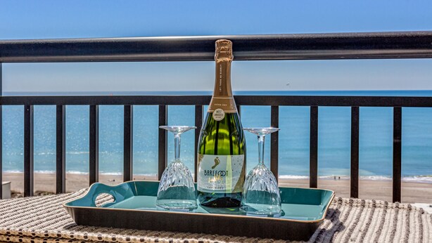 Een fles Barefoot wijn en twee wijnglazen op een dienblad, bij een balkon met uitzicht op het strand.