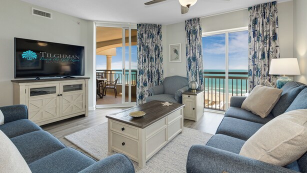 A living room with a TV, sofas, a coffee table, and a view of the ocean.