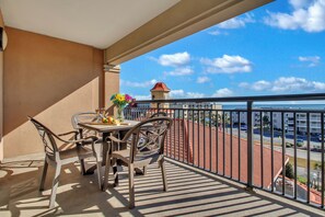 A balcony with a table and chairs, a vase of flowers, and a view of a building with a red roof. - 3BR- 5th floor Oceanview condo|Short walk to beach (North Myrtle Beach)