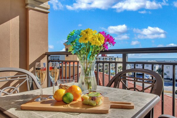 A table with a vase of flowers, two glasses of champagne, a fruit bowl, and a wooden board. - 3BR- 5th floor Oceanview condo|Short walk to beach (North Myrtle Beach)