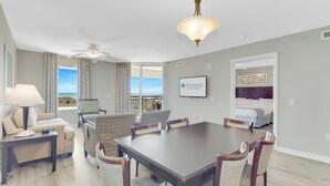 Un salon spacieux avec une grande table à manger, des sièges confortables, un ventilateur de plafond et une vue sur l’extérieur.