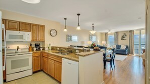 A modern kitchen with wooden cabinets, a microwave, and a dishwasher. There is a dining area with a table and chairs, and a living room with a sofa and a view of the outdoors. - 3BR-6th floor North Oceanview condo|Close to beach (North Myrtle Beach)