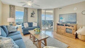 A living room with a sofa, a coffee table with flowers, a TV, and a balcony with a view. - 3BR-6th floor North Oceanview condo|Close to beach (North Myrtle Beach)