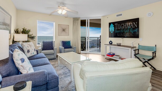 A living room with a sofa, armchair, and a television displaying 'Tilghman Beach & Golf Resort'. - 3BR- 8th floor- Oceanview condo| Short walk to beach| Resort Access| (North Myrtle Beach)