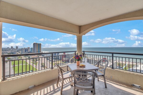 Varanda com mesa e cadeiras, com vista para a praia e o horizonte da cidade.