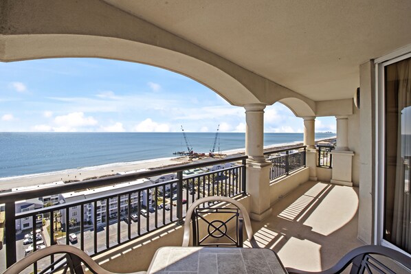 Enjoy the ocean view from this balcony with a table and two chairs, surrounded by a structured design featuring arches and columns.