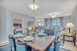 A dining area with a large table set for four, a sofa, and a lamp.