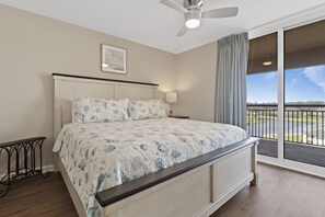 A bedroom with a large bed, a ceiling fan, a nightstand with a lamp, and a view of the outdoors through a sliding glass door.