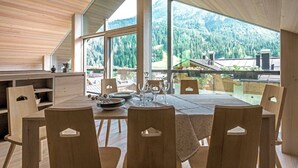 A dining area with a large table and chairs, large windows offering a view of a forested mountain range.