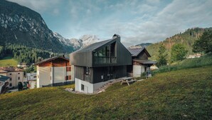 A modern house with a sloped roof, large windows, and a view of mountains.