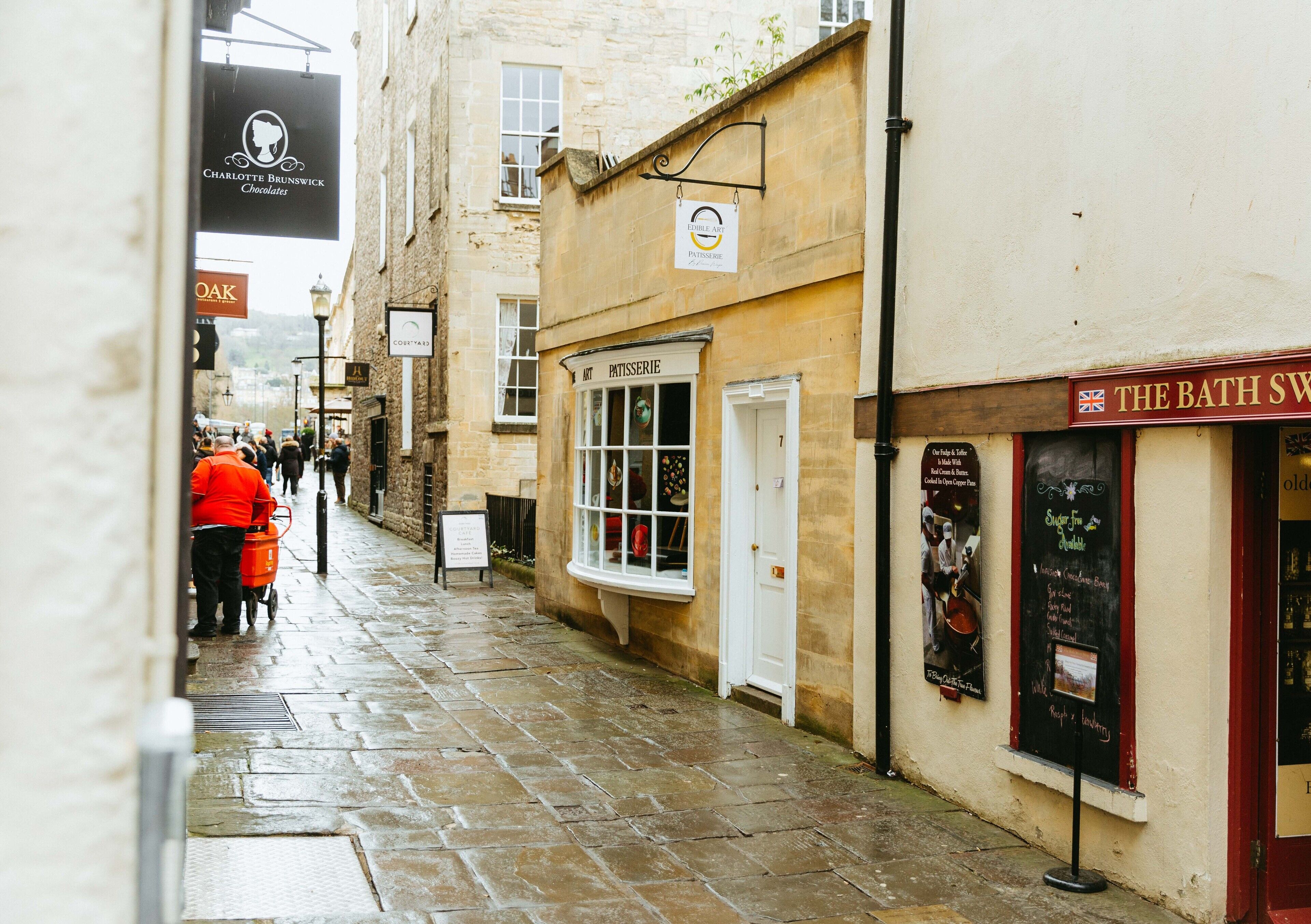 A narrow street with shops, including a patisserie and a chocolate shop.