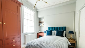 Un dormitorio con un armario grande, una cama con cabecera azul, mesitas de noche con lámparas y una ventana con vistas.