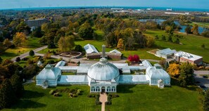 Luchtbeeld van een grote kas met een centrale koepel, omgeven door gazons en bomen.