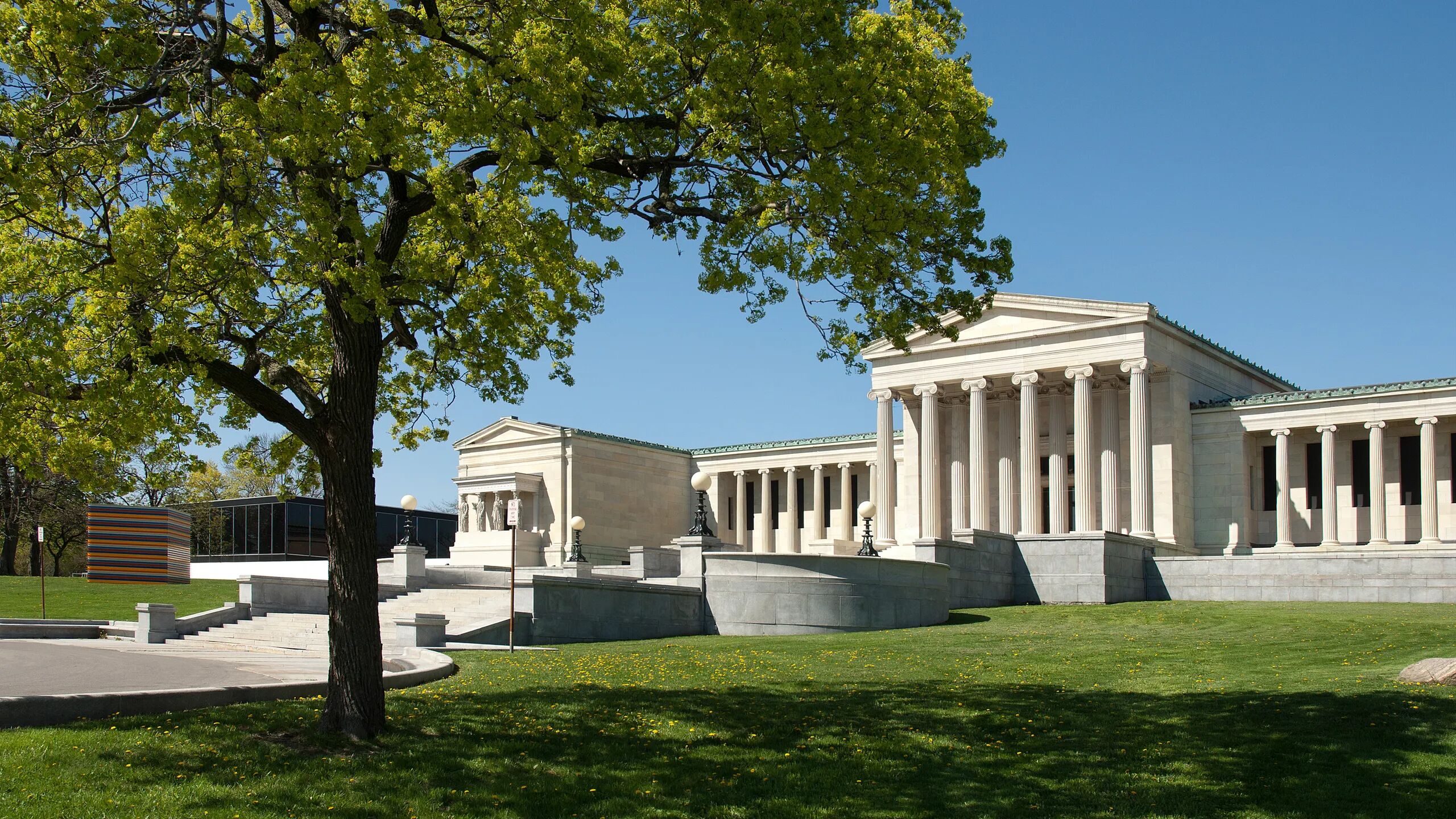 A classical building with columns and a central pediment, surrounded by a well-maintained lawn and a tree.
