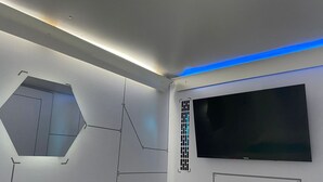 Une chambre moderne dotée d’un grand téléviseur à écran plat fixé au mur, d’une fenêtre hexagonale et d’un lit avec une tête de lit.