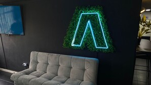 Un intérieur moderne avec un canapé gris, un néon vert en forme de « A » et un téléviseur fixé au mur.