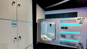 Une pièce futuriste comprenant un lit, un panneau de contrôle et une porte avec des casiers numérotés.