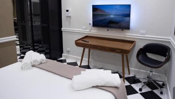 Ein Hotelzimmer mit einem Bett, einem an der Wand befestigten Fernseher, einem Schreibtisch mit Stuhl und einem Schachbrettmuster-Boden.