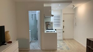Een moderne keuken met witte kasten en een klein eiland, een gang naar een badkamer en een deur naar een andere kamer.