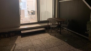 Een klein terras met een tafel en stoelen, een schuifdeur naar een balkon en een trap naar de bovenverdieping.