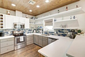 Une cuisine moderne dotée d’appareils électroménagers en acier inoxydable, de meubles blancs et d’un dosseret carrelé bleu.