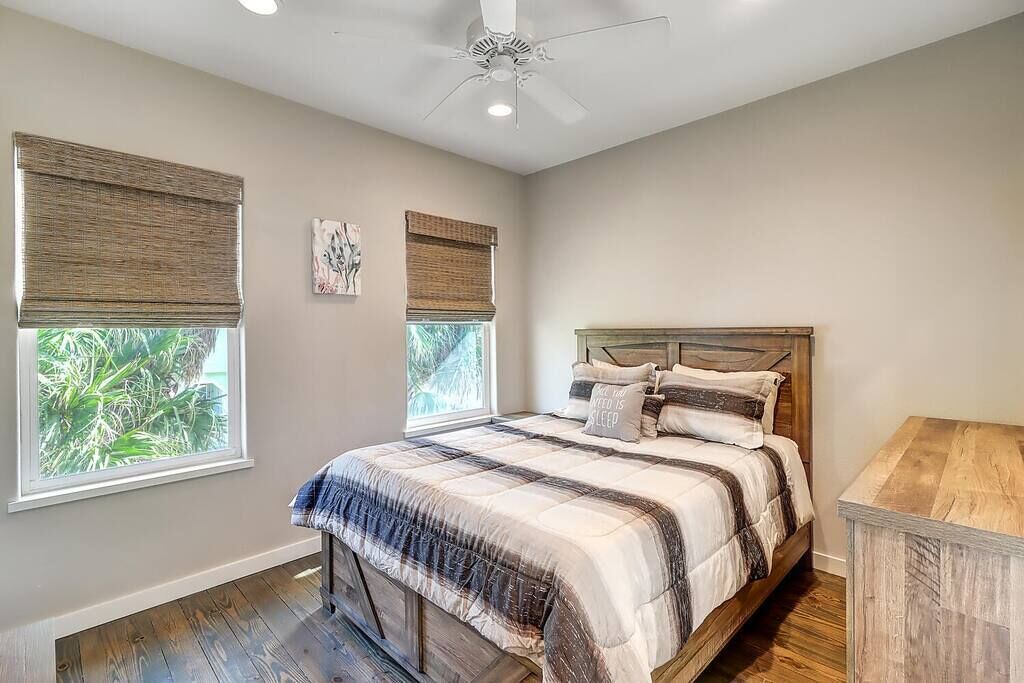A bedroom with a bed, a ceiling fan, and two windows with blinds.