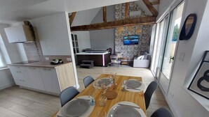 Une cuisine moderne avec des meubles blancs, une table à manger en bois pour quatre personnes et un coin salon avec un canapé et un téléviseur.