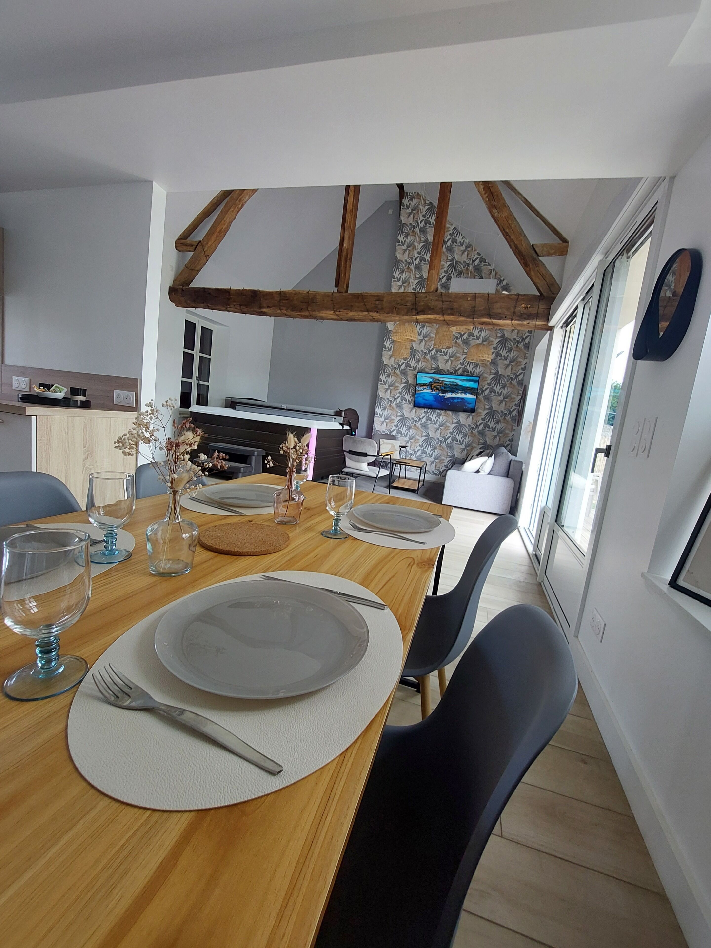 Un comedor con una mesa de madera preparada para cuatro personas, una chimenea y una cocina al fondo.