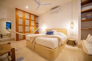 Une chambre à coucher avec un lit, une armoire en bois, un miroir, un hamac et un ventilateur de plafond.