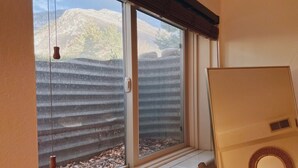 Habitación con ventana que da a un patio trasero con valla de madera y vistas a la montaña.