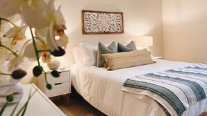 Un dormitorio ordenado con cama, almohadas, una lámpara de noche y un adorno de pared.