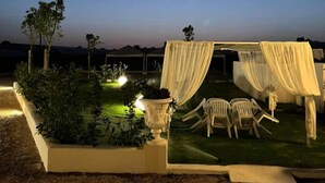 An outdoor seating area with white chairs and a canopy, surrounded by greenery and a clear sky. - ATENA APPARTAMENTO PER 5 PERSONE (Lazio)