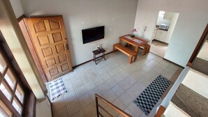 A spacious living area with a wooden door, a flat-screen TV mounted on the wall, a wooden dining table with benches, and a tiled floor. - Condomínio Santa Mônica (Belo Horizonte)
