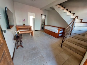 A room with a bed, a wooden bench, a small table with a vase, and a staircase. - Condomínio Santa Mônica (Belo Horizonte)