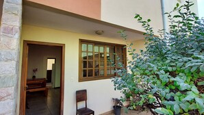 A building with a tiled patio, a wooden bench, a potted plant, and a doorway leading inside. - Condomínio Santa Mônica (Belo Horizonte)