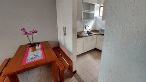 A small kitchen with white cabinets, a wooden table with a vase of flowers, and a tiled floor. - Condomínio Santa Mônica (Belo Horizonte)