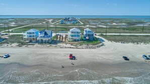 Ett flygbildsfoto av en fastighet vid kusten med flera blå byggnader, en sandstrand och fri utsikt över havet.