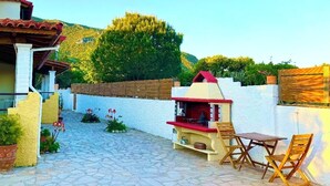 A patio with stone flooring, a small barbecue area, and outdoor seating. - AHP (Corfu)