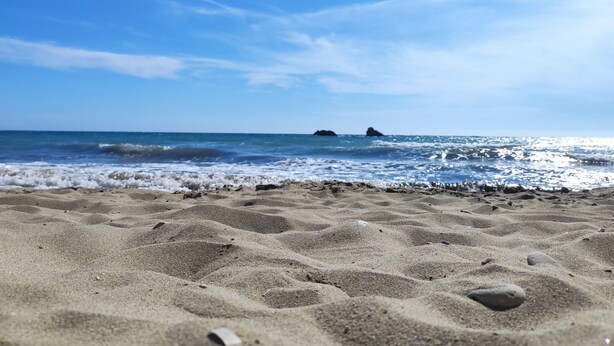 A sandy beach with gentle waves and distant rocky outcrops under a clear blue sky. - AHP (Corfu)