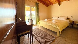 A bedroom with a bed, a desk, and a chair. There is a window with curtains and a view of the outside. - AHP (Corfu)