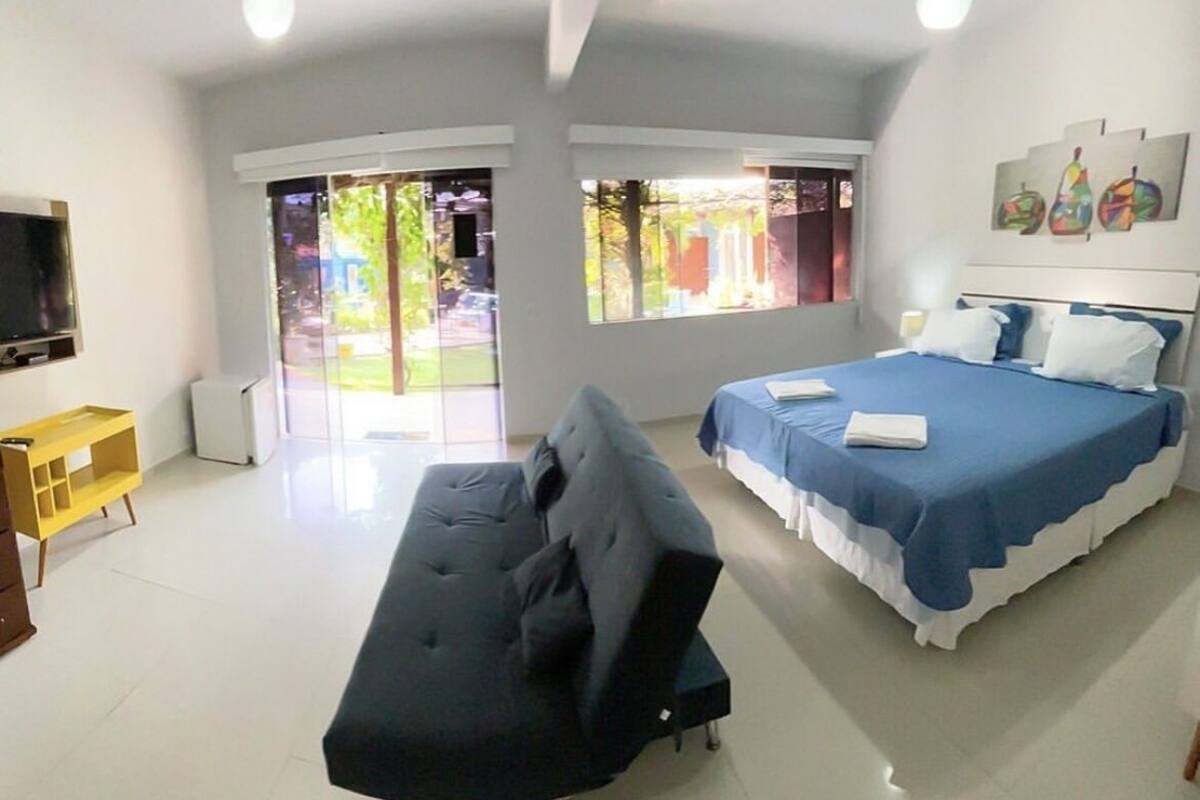 Ein modernes Hotelzimmer mit einer Couch, einem Bett mit blauer Bettwäsche, einem Fernseher und großen Fenstern mit Blick ins Freie.