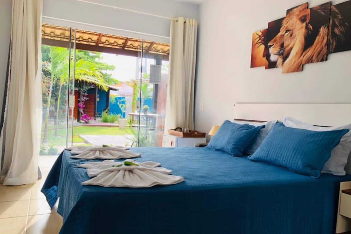 Ein Schlafzimmer mit einem großen Bett, Blick auf einen Garten und einem Löwenbild an der Wand.