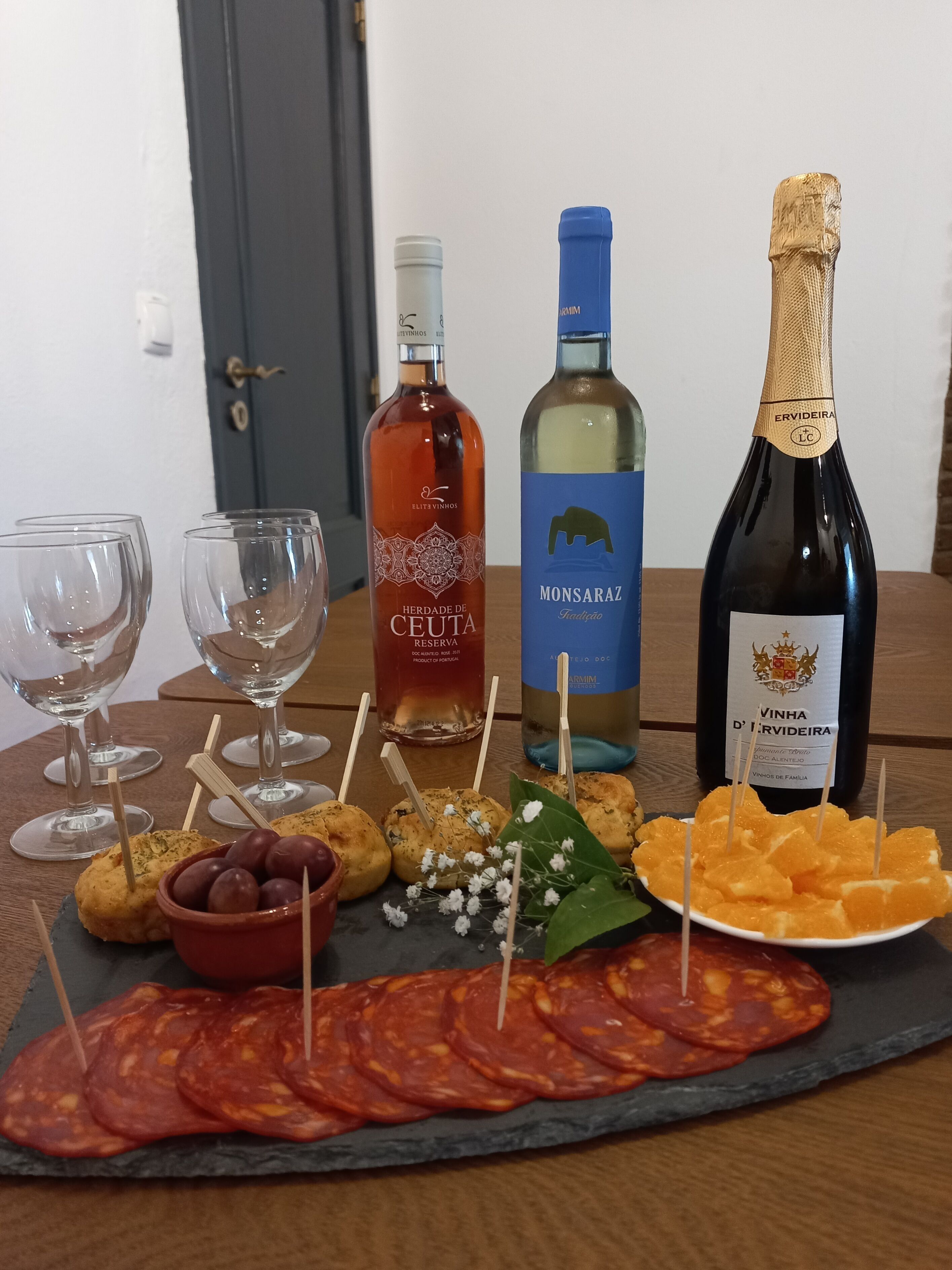 A table with a variety of food items and three bottles of wine.
