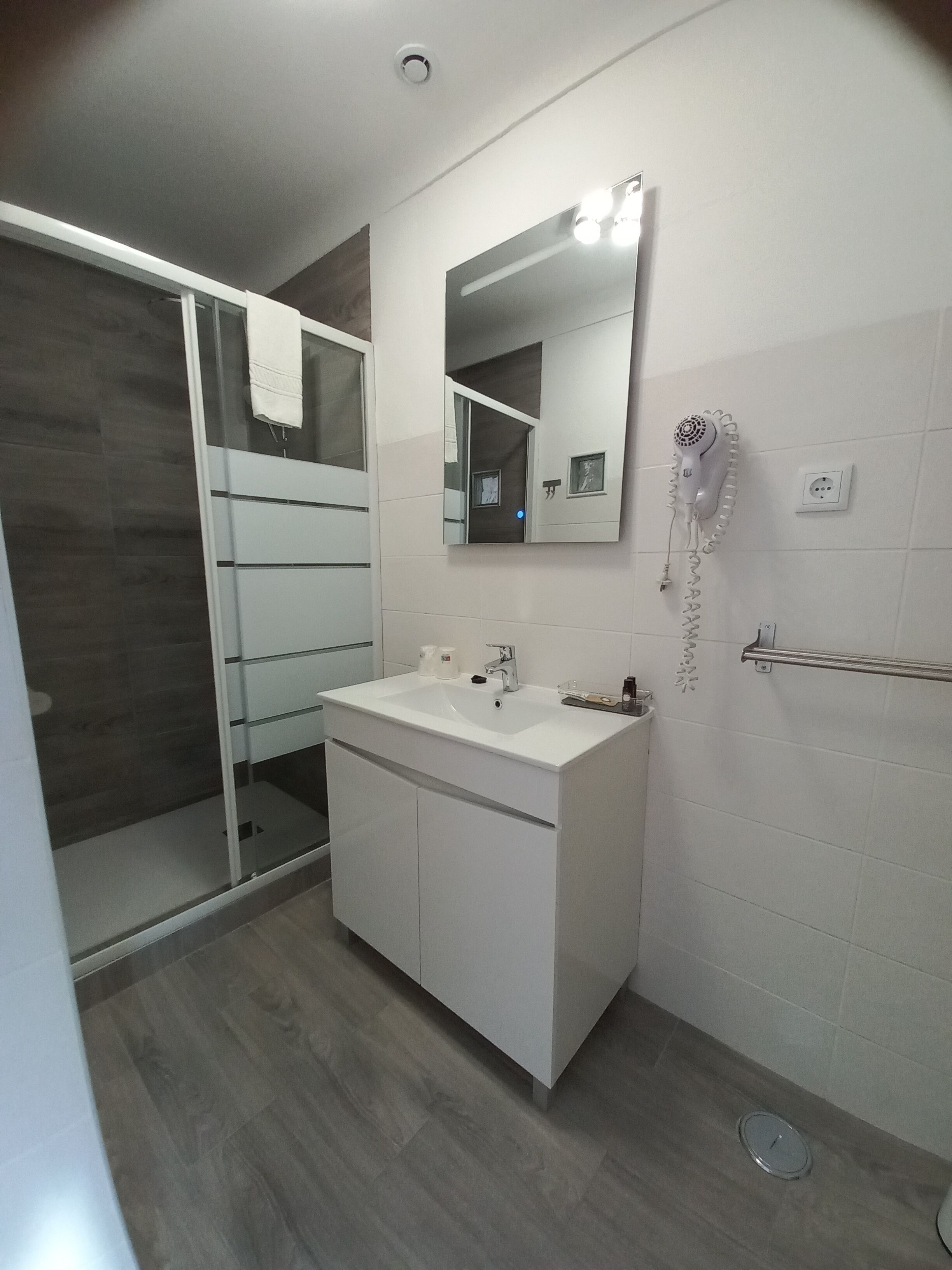 Un baño moderno con un tocador blanco, una cabina de ducha de vidrio y un secador de pelo montado en la pared.